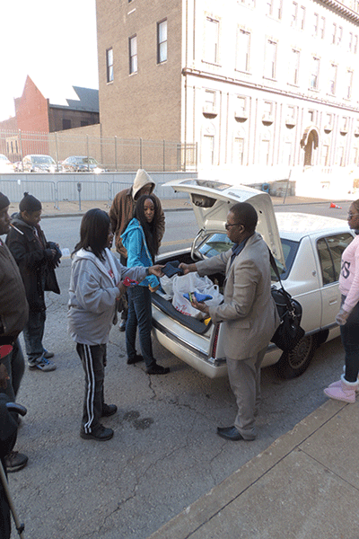 Volunteers Lushomo Chambwa and Jasmine Brown, standing by trunk, give supplies to people outside New Life Evangelistic Center in St. Louis. (Photo by Carl Anderson)