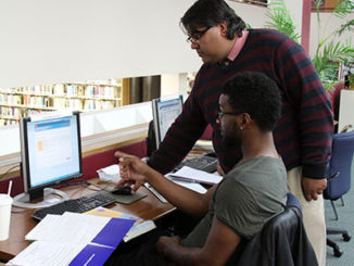 Librarian Neil E. Das, top, helps civil engineering student Timotheus Paulette, 23, with a campus computer. (Photo by Tina Alberico)