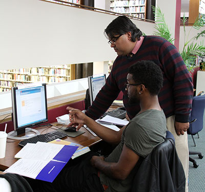 Librarian Neil E. Das, top, helps civil engineering student Timotheus Paulette, 23, with a campus computer. (Photo by Tina Alberico)