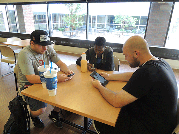 Business major Spencer Ahpeatone, 20, left to right, fine arts major Coride Arrington, 22, and network engineering major Joshua Dellacroce, 20, use their hand-held devices. (Photo by Don Dixon)