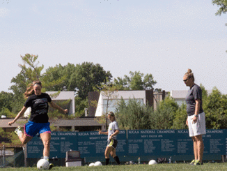 New soccer coach Erin Hesselbach, right, looks on as Emily Fox, left, kicks the ball and Sarah Fuller waits her turn during a “shoot-around” (pre-practice) on the Meramec campus last week. (Photo by Evan Sandel)