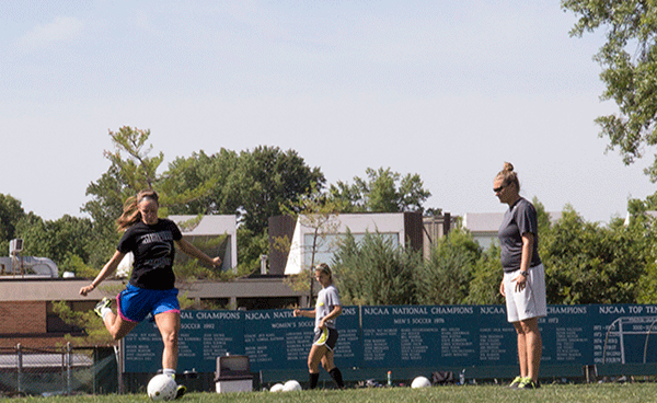  New soccer coach Erin Hesselbach, right, looks on as Emily Fox, left, kicks the ball and Sarah Fuller waits her turn during a “shoot-around” (pre-practice) on the Meramec campus last week. (Photo by Evan Sandel)