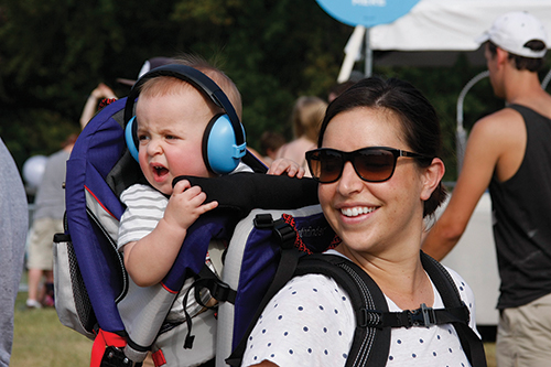 Andrew Hurley, 11 months, wears headphones while riding on Mom Cara Hurley’s back at LouFest. (Photo by Julian Hadley)