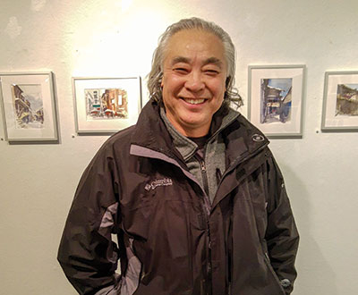 Yingxue Zuo, an art professor at Forest Park, poses in front of some of his watercolor paintings.