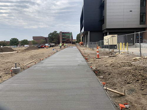 Workers are shown in the early stages of installing a concrete walkway that will become part of Forest Park’s new quad, south of the Center for Nursing and Health Sciences. This summer, A and B Towers were demolished to make way for it. (Photo by Casaan Whitney)