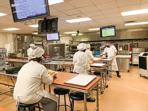 Students wear masks and practice social distancing as Chef Martin Lopez, right, leads a baking and pastry class in the Hospitality Studies kitchen at Forest Park. (Photo by Cassan Whitney)