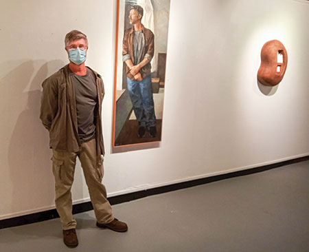 Art professor Dan Wine stands next to his self-portrait oil painting titled “Waiting” in the Gallery of Contemporary Art. At right is a sculpture by Norleen Nosri, chair of the visual and performing arts department, titled “Duo Solo.” (Photo by Theodore Geigle)